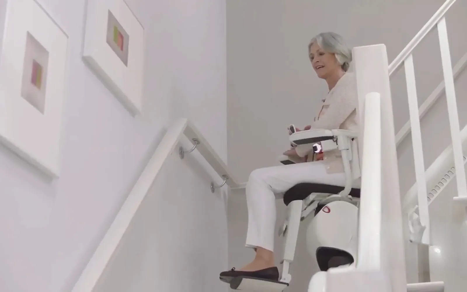 Femme souriante assise sur un fauteuil monte-escalier qui gravit un escalier blanc (Audun-le-Tiche, Moselle)