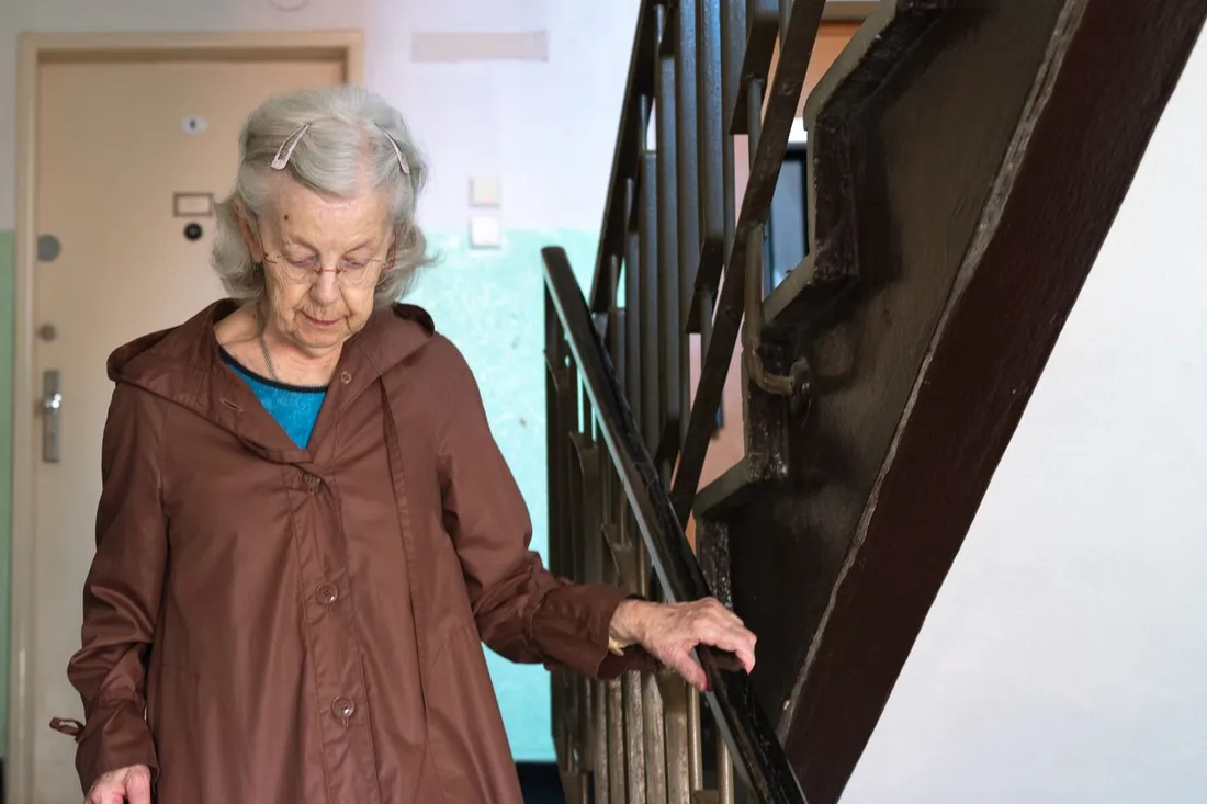 Femme âgée qui descend l'escalier de son immeuble en tenant la rampe (Aydat, Puy-de-Dôme)