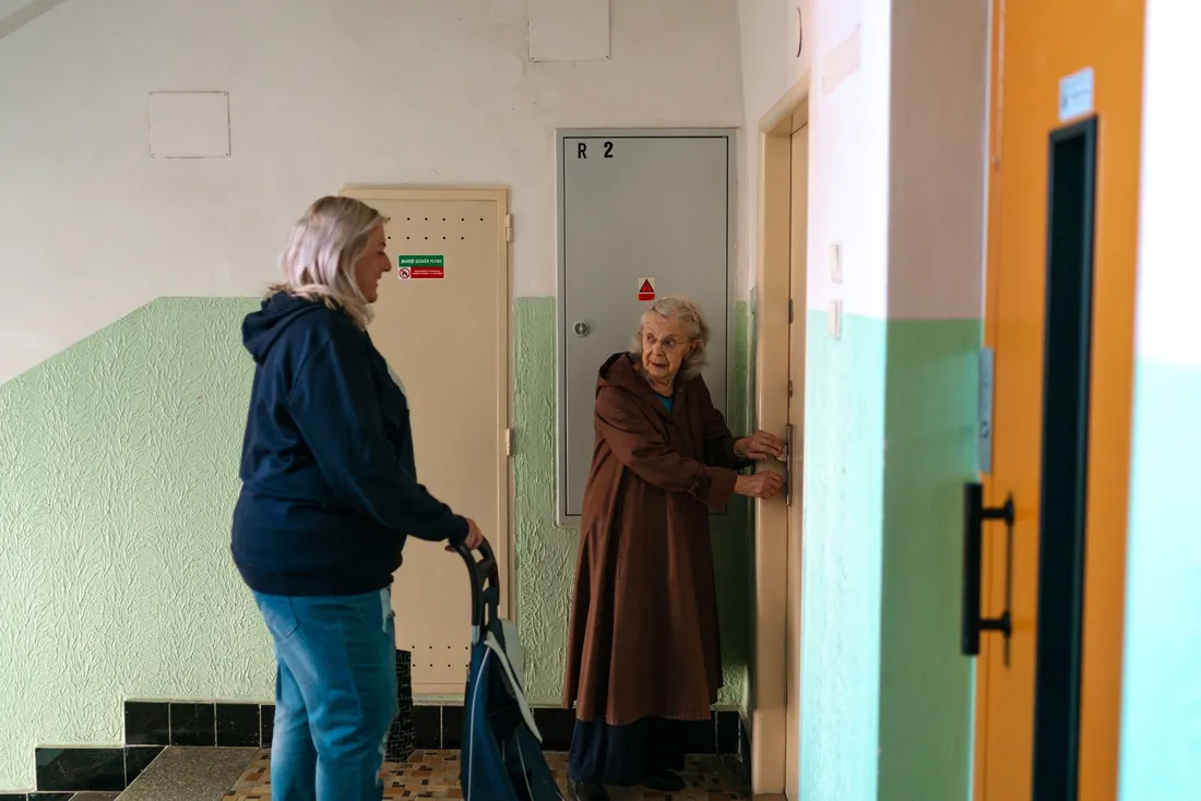 Femme âgée à la porte de son appartement, sa fille à côté d'elle sur le palier (Orschwihr, Haut-Rhin)