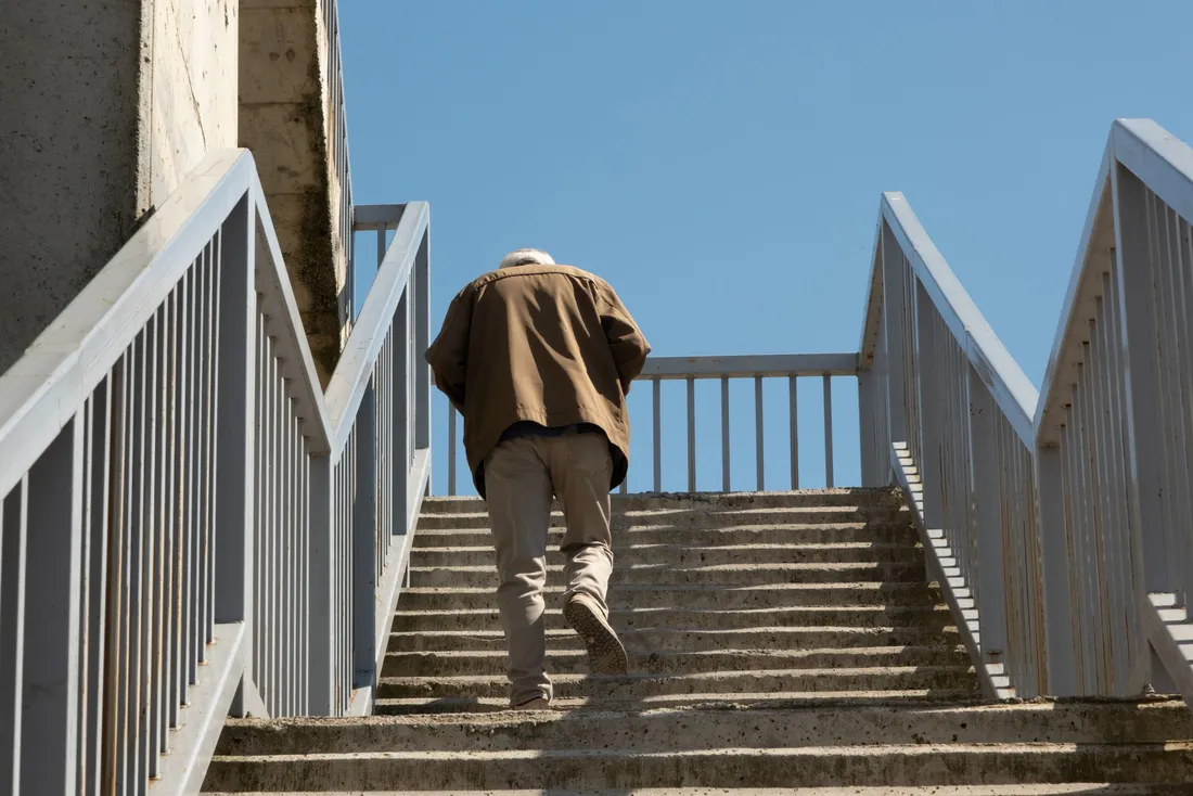 Homme âgé de dos qui gravit un long escalier extérieur à garde-corps (Écrouves, Meurthe-et-Moselle)
